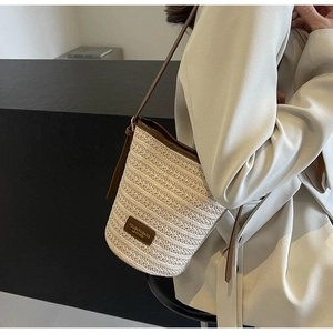 Detailed close-up of woven straw texture and premium brown leather trim on bucket bag