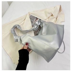 Detail view of metallic silver tote bag with pleated handle on a beige blazer