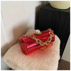 Detail of red acrylic cylindrical evening bag with pearl clasp and gold chain on knit fabric