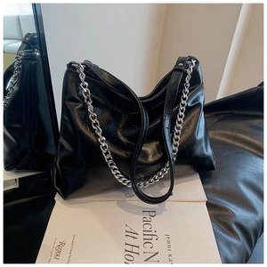 Detail of black glossy leather tote bag with silver chain strap and adjustable leather belt