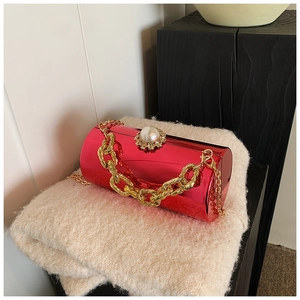 Detail of red cylindrical evening clutch with pearl clasp and gold chain straps