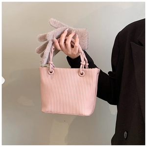 Detail of pink pleated bucket bag with knotted handles shown against a dark coat