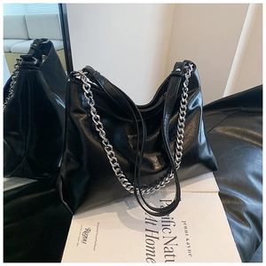 Detail of the black glossy leather tote featuring a thick silver chain and smooth texture