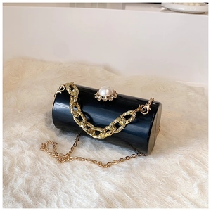 Detailed view of black cylinder bag with large pearl clasp and golden link chains