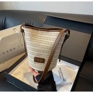Detail of hand-woven cream straw bucket bag with dark brown leather trim and logo