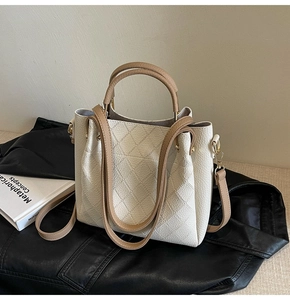 Detailed view of cream-colored bucket bag with diamond quilting and khaki brown handles