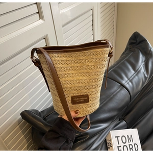 Close-up of woven beige straw texture and dark brown leather trim on the bucket bag