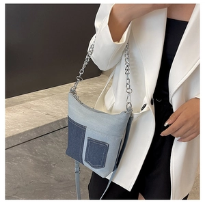 Detail of blue denim bucket bag with silver chain strap worn over a white blazer