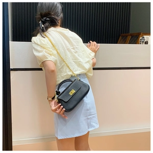 Detail of black crossbody bag with gold chain strap and square metal lock on model
