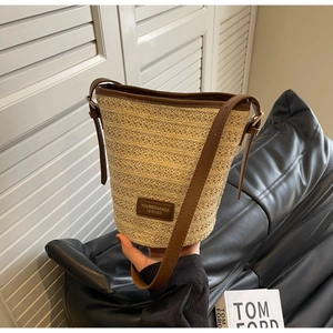 Close-up of woven straw bucket bag with brown leather trim and embossed brand label