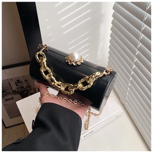 Detail of black acrylic cylinder clutch with large pearl clasp and gold chain strap