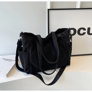 Detail of black corduroy tote bag showing side pockets and adjustable shoulder strap