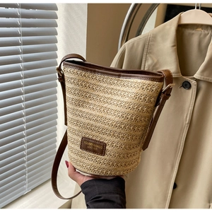 Detail of handwoven straw bucket bag with dark brown leather trim and shoulder strap