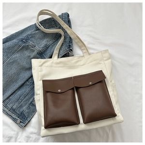 Detail of white canvas tote bag featuring brown leather pockets and metal snap buttons