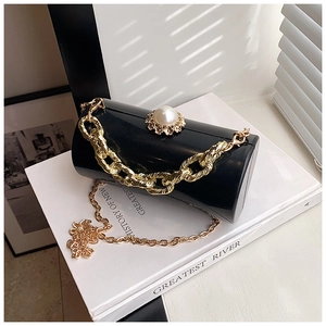 Close-up of black cylinder bag with large pearl clasp and golden chain strap detail