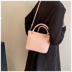 Detail of pink pleated bucket bag with vertical stripes and woven handles on black coat