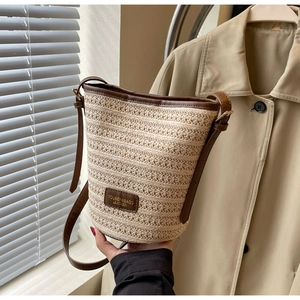 Close-up of hand holding a woven straw bucket bag with brown leather trim details