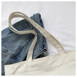 Minimalist cream canvas tote bag detail with wide shoulder straps on denim background