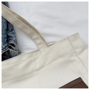 Detailed close-up of cream canvas tote bag showing stitching and brown leather patch