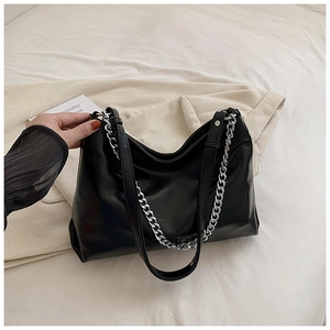 Close-up of black glossy leather tote featuring chunky silver chain and adjustable strap