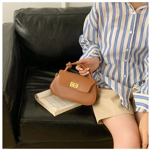 Detail view of brown crossbody bag with a gold twist lock and knotted handle on a sofa