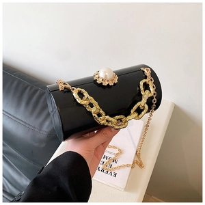 Detail of black acrylic cylindrical clutch with pearl clasp and golden chain straps