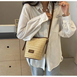 Close-up of woven straw bucket bag with dark brown leather trim and adjustable strap
