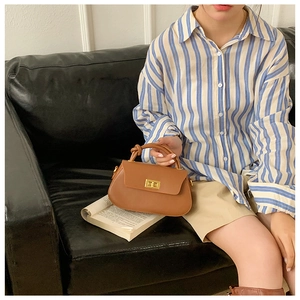Detail of a brown leather handbag with a gold twist lock and unique knotted handle on a book