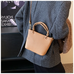 Detailed view of camel pleated bucket bag styled with a grey herringbone blazer