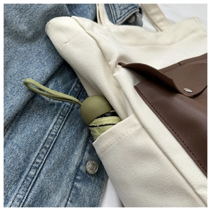 Detail view of canvas tote bag with brown leather pocket and side umbrella compartment