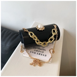 Detail of black acrylic cylindrical evening bag with large pearl clasp and gold chains