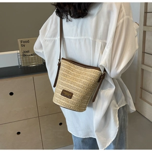 Detailed close-up of woven straw bucket bag with leather trim and branded logo patch