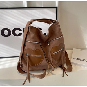 Detail of a brown canvas backpack featuring heart-shaped leather pockets and silver zippers