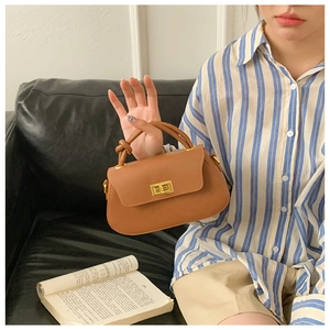 Detailed macro shot of brown leather handbag featuring a golden metallic twist lock closure
