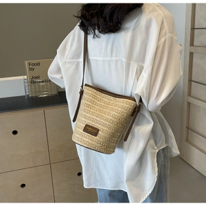 Detail of woven straw bucket bag with brown leather trim and adjustable crossbody strap