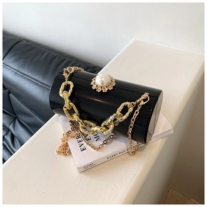 Detail of black acrylic cylinder bag with pearl ornament and gold chain straps