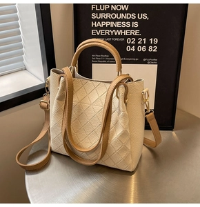 Close-up of quilted cream bucket bag with contrasting tan handle and gold-tone hardware