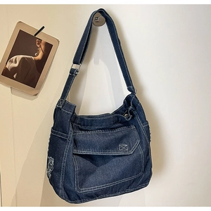 Dettaglio della borsa a tracolla in denim blu scuro con cuciture bianche a contrasto e tasche