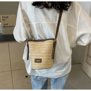 Detail of hand-woven straw bucket bag with dark brown leather straps on a model