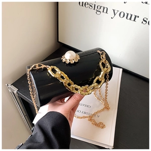 Detail of black acrylic cylinder clutch with pearl clasp and gold floral metal accents