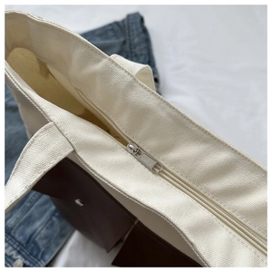 Close-up of metal zipper closure and canvas texture on cream tote bag with brown pocket