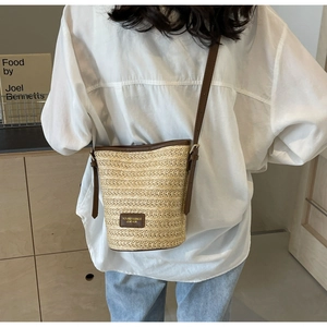 Detail of woven straw bucket bag featuring dark brown leather trim and shoulder strap