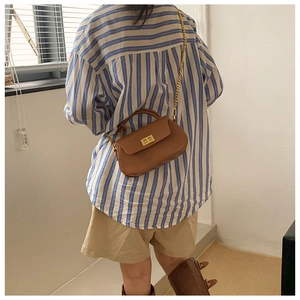 Brown leather crossbody bag with gold chain and metal lock shown in an outdoor lifestyle view