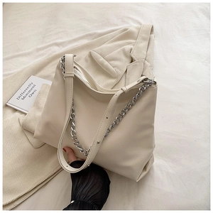Detail of a beige tote bag with a chunky silver chain and leather strap on a soft jacket