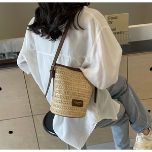 Detail of woven straw bucket bag with dark brown leather trim and adjustable shoulder strap