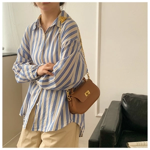 Detail view of brown leather crossbody bag with gold metal chain and rotary lock