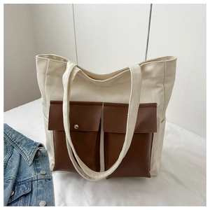 Detail of canvas tote bag featuring dual brown faux leather pockets and sturdy straps