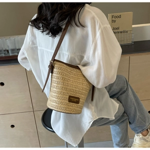 Detail of hand-woven straw bucket bag with brown leather trim and adjustable strap