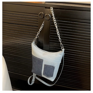 Detail of blue denim bucket bag with silver chain strap and bicolor patchwork design