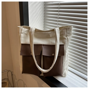 Detailed view of canvas tote bag with brown faux leather pockets and metal buckle hardware